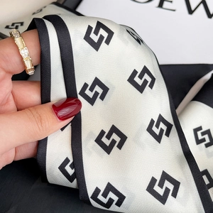 Close-up of a narrow silk scarf with black geometric S-pattern and smooth texture