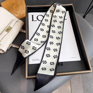 Detail of narrow geometric silk scarf styled over a luxury magazine and leather handbag