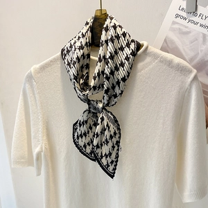 Détail d'un foulard en soie plissé pied-de-poule noir et blanc sur un tricot blanc