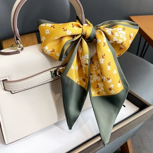 Detail of floral silk scarf tied on beige leather handbag with metal lock closure