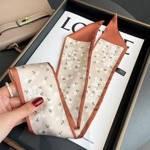 Detail of floral skinny scarf with orange border tied on a luxury beige handbag