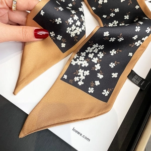 Close-up of a floral skinny silk scarf with black and gold satin finish tied on a hand
