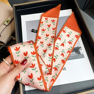 Détail d'un foulard étroit à motif floral noué sur un sac avec bordure orange vif