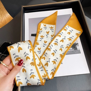 Détail d'un foulard twilly en soie à motif floral jaune gingembre sur une boîte cadeau noire