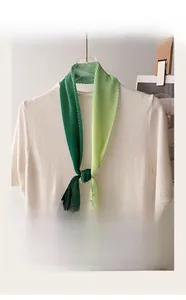 Detail view of a green gradient pleated skinny scarf styled on a white knitted top neckline