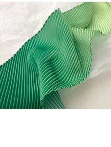 Detail of green gradient pleated scarf fabric showing fine vertical accordion texture