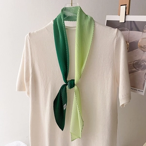 Green gradient pleated silk scarf accessory tied on a cream knitted sweater neck