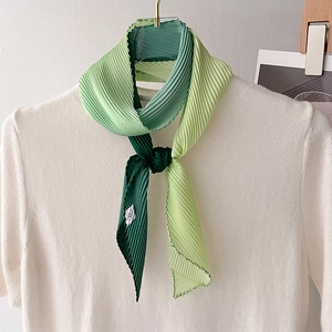 Detail of green pleated scarf showing gradient texture and stitching on white knitwear