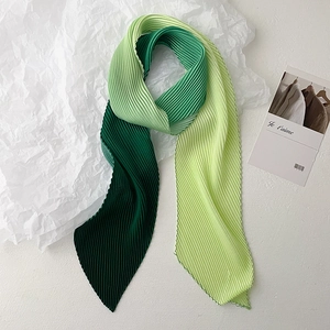 Detail of gradient green pleated skinny scarf showing fine accordion texture on white paper