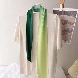 Detail of green gradient pleated skinny scarf tied on a white knit shirt neck