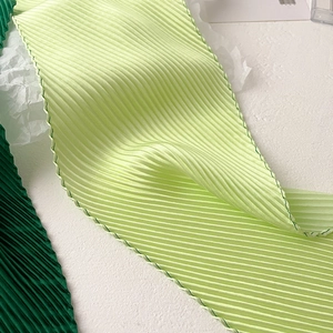 Close-up of light green pleated scarf fabric with vertical folds and dark green stitching