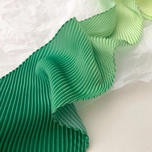 Close-up of green gradient accordion pleats on lightweight silk accessory fabric