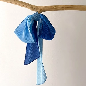 Close-up of pleated silk scarf with blue gradient tied on a natural wood branch