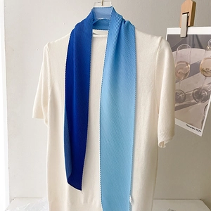 Detail of blue gradient pleated skinny scarf tied on a white knitted sweater