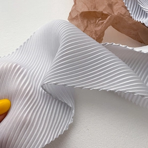 Detailed close-up of white pleated silk scarf fabric showing fine vertical textures