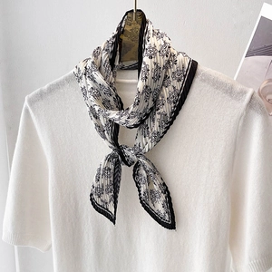 Foulard plissé en soie noir et blanc à motif paisley porté sur un pull en maille blanche