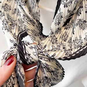 Détail d'un foulard en soie plissé avec motif paisley noir et nœud élégant à la main