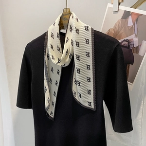 Pleated black and white silk scarf with artistic letter pattern on a black sweater