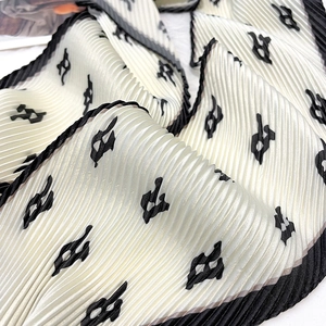 Close-up of pleated beige silk scarf featuring black geometric patterns and fine edges