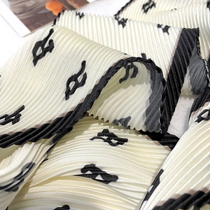 Detailed close-up of pleated silk scarf featuring black letter print and elegant textures