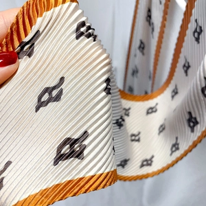 Close-up of pleated silk scarf with black letter print and orange edge stitching