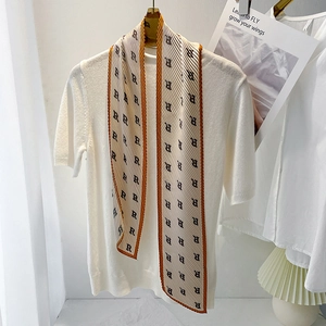 Detail of pleated silk scarf with letter R print and orange borders on a white hanger