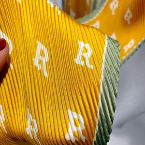 Macro shot of accordion pleated silk scarf with yellow and green contrast and R logo