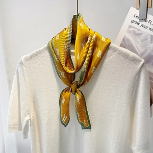Bright yellow pleated silk scarf with letter print and dark green border on white sweater