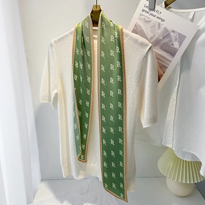 Elegant green pleated silk scarf with white letter pattern on white knitted sweater