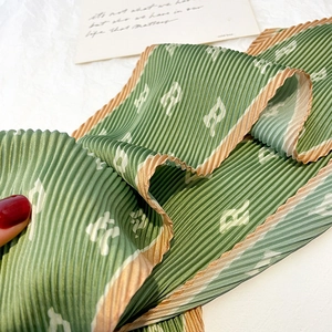 Detail of green pleated silk scarf with white R letter print and orange border