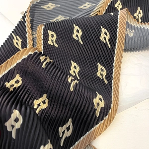 Detail of accordion pleated silk scarf with monogram R pattern and golden borders