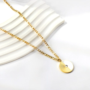 Detail of gold disc pendant featuring sunray texture, white shell inlay and zircon stone