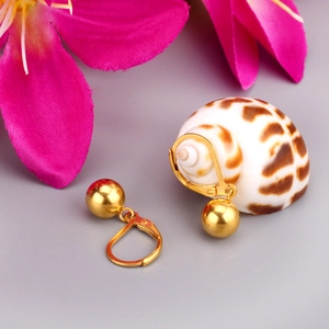 Boucles d'oreilles boules dorées avec fermoir à levier sur un fond minimaliste chic