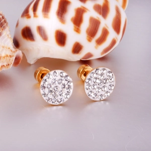 Close-up of golden round stud earrings with shimmering rhinestones on a seashell