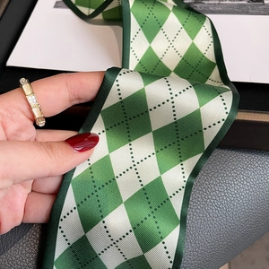 Close-up of a green diamond pattern satin neckerchief and a gold geometric ring