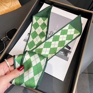 Detail of green diamond pattern silk scarf on black tray with fashion accessories