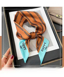 Detail of orange striped twilly scarf with blue tip and crown accent on black tray