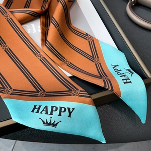 Detail of orange and blue silk scarf with stripes and crown logo on a dark tray