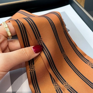 Close-up of luxury orange silk scarf with black stripes and logo, showing soft texture