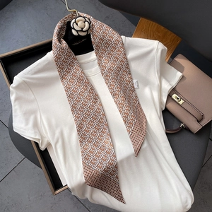 Detail of a geometric silk scarf with a camellia brooch on a white T-shirt