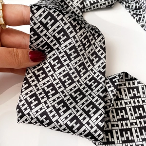 Detailed shot of black and white silk scarf featuring geometric H patterns and satin texture