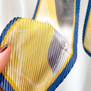 Détail de la texture d'un foulard en soie plissé aux motifs jaunes et bleus