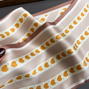 Détail d'une écharpe en satin aux rayures champagne et motifs floraux de couleur orange