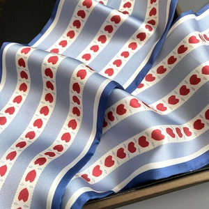 Détail d'un foulard en satin bleu clair avec motifs de cœurs rouges et bords rayés
