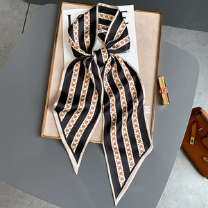 Foulard en soie à motifs cœurs orange et rayures noires noué sur un sac en cuir