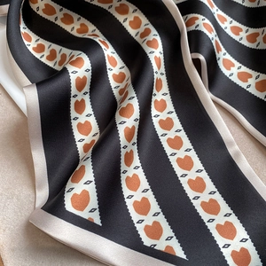 Détail d'un foulard long en satin à rayures noires et blanches et motifs cœurs oranges