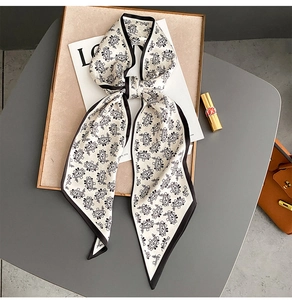 Detail of white paisley silk scarf tied in a bow on a luxury wooden display tray