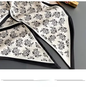 Detailed close-up of beige paisley silk scarf with black borders and smooth texture
