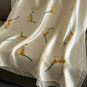 Off-white silk scarf with orange calla lily print draped on dark leather background