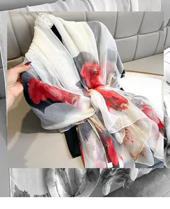 Detail of floral silk scarf with red flowers on cream base and camellia accessory